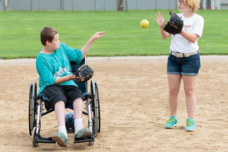 Junior high student in a wheel chair playing catch with softball and glove with classmate.