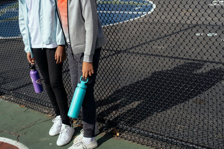 two teenagers holding water bottles on an outdoor athletic court